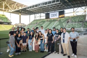 A group of IBM workers, including Kassidy Saba, gathered for a picture together in a sports arena.